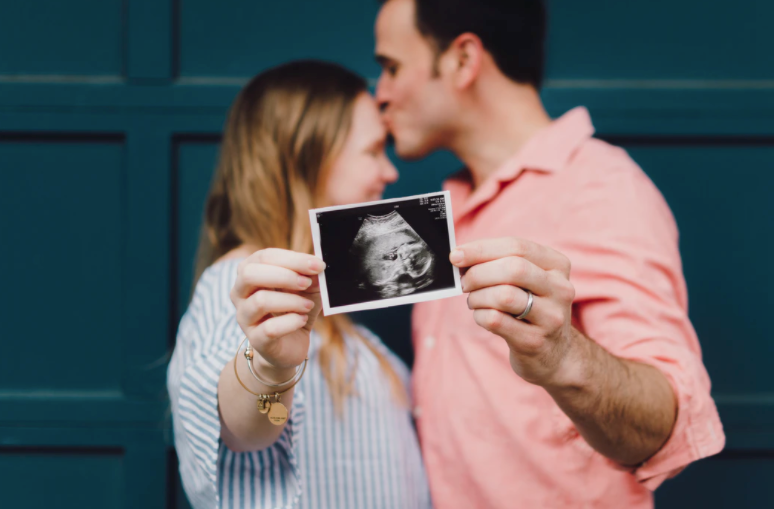 a couple getting ready for a Babymoon trip and holding an ultrasound