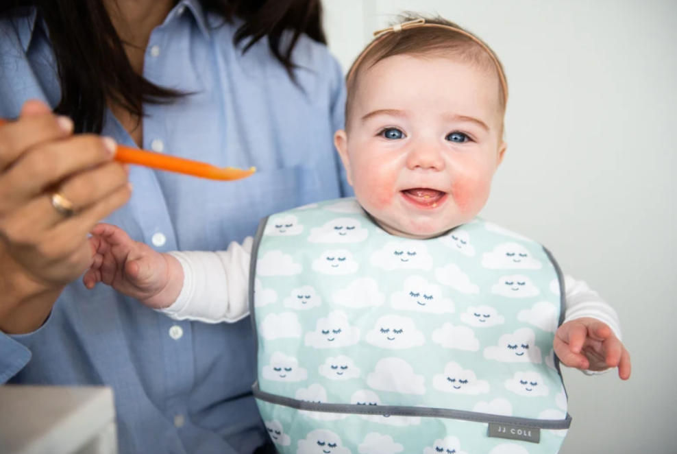 smiling baby about to be fed by Mom with a spoon of food